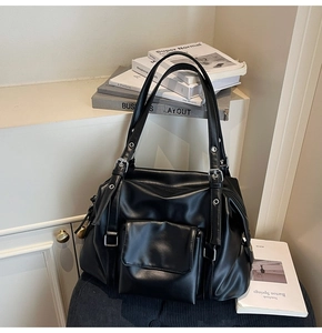 Detail of black faux leather tote bag showing silver metal buckles and front pocket