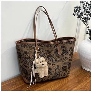 Close-up of vintage paisley print tote bag with plush puppy charm on wooden table