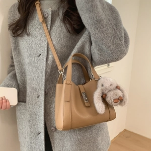 Close-up of caramel leather bucket bag with plush rabbit charm and metal buckle