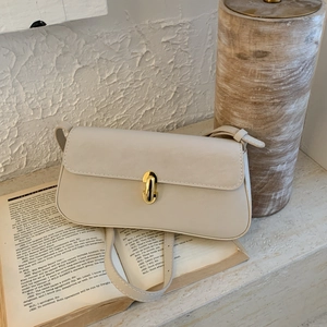 Detailed close-up of cream leather shoulder bag with golden U-shaped buckle on vintage books