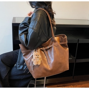 Detail of a large brown tote bag showing supple leather texture and bear plush charm