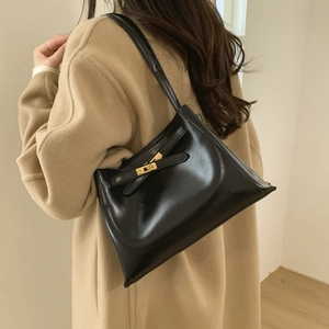 Detail of a black glossy leather shoulder bag with gold metal buckle on camel coat