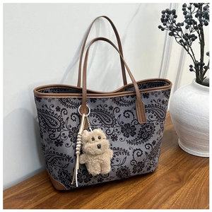 Detail of vintage paisley print tote bag with brown leather trim and plush puppy charm