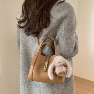 Close-up of camel leather bucket bag with silver buckle and plush rabbit charm on a grey coat