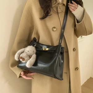 Detail of black glossy bucket bag with golden twist lock and plush bunny charm accessory