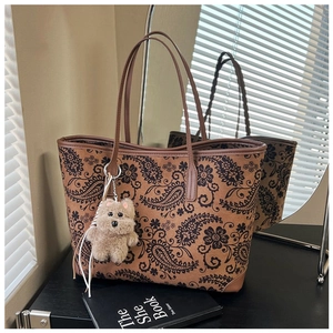 Close-up of vintage brown floral tote bag with a cute plush dog charm on a dark desk