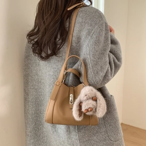 Detail of khaki leather bucket bag with metal lock and cute plush bunny charm