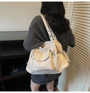 Detail of white tote bag featuring adjustable buckle straps and a decorative fringe tassel