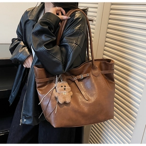 Close-up of brown PU leather tote bag featuring a decorative buckle and plush bear charm