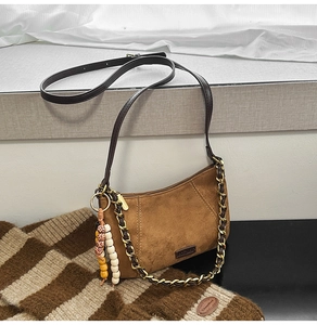 Detailed view of brown suede shoulder bag with chain strap and beaded tassel charm