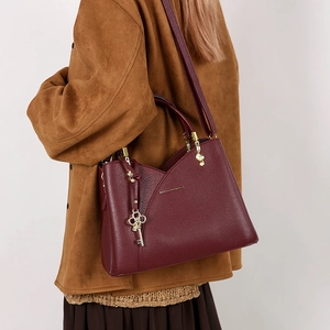 Side view of a burgundy lychee leather bucket bag with a gold key charm on a model