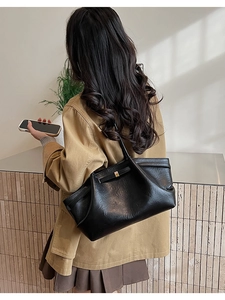 Détail du sac cabas vintage en cuir brillant noir porté avec boucle dorée