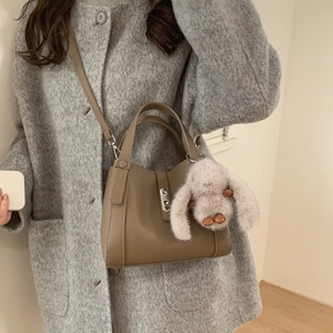 Detailed view of khaki leather bucket bag with silver buckle and plush rabbit charm