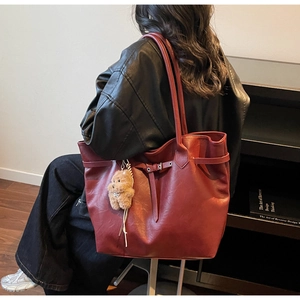 Detail of burgundy leather tote bag with side buckle and plush bear pendant on shoulder