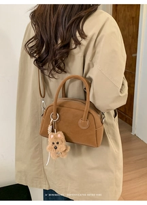 Dettaglio della borsa marrone opaca con manici rotondi e accessorio orsetto di peluche