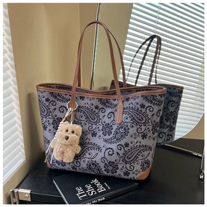 Detail of vintage paisley tote bag with dark leather trim and plush bear charm accent