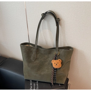 Détail d'un sac cabas vert olive à texture mate avec pendentif décoratif en forme d'ours