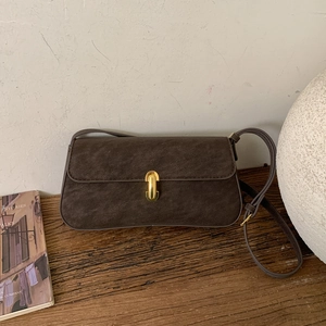 Detail of dark brown faux suede bag featuring a gold horseshoe buckle on the front flap