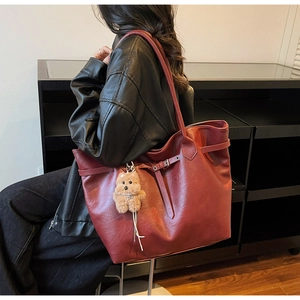 Side view of burgundy matte leather tote bag with decorative buckle and plush dog charm