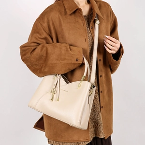 Detail of cream crossbody bucket bag with litchi texture and gold charms on model