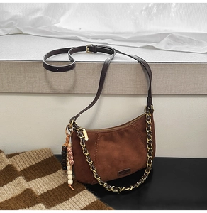 Close-up of brown suede shoulder bag with gold chain strap and boho beaded pendant charm