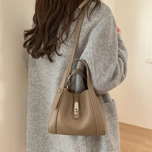 Detail of taupe pebbled leather bucket bag featuring a silver twist lock on the front flap