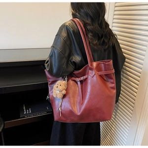 Detail shot of a large burgundy tote bag in premium faux leather with a cute plush charm