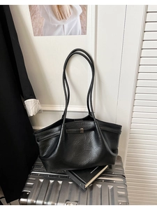 Détail d'un grand sac cabas noir en cuir avec boucle dorée posé sur une valise