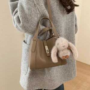 Brown lychee leather bucket bag with silver lock and plush bunny charm on a model