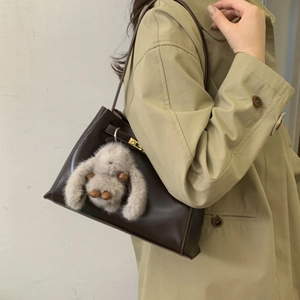 Detail of vintage brown bucket bag with gold lock and cute plush bunny charm