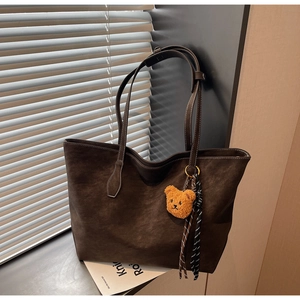 Détail d'un sac cabas marron foncé mat avec pendentif ours et ruban à carreaux