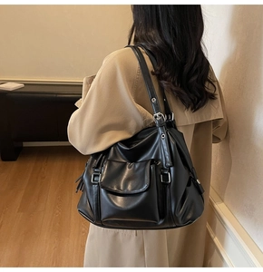 Detail of a large black vintage tote bag with metal buckles on a trench coat model