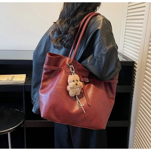 Close-up of burgundy tote bag with leather strap detail and plush dog charm