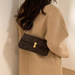 Detail of a dark brown suede underarm bag with a golden U-shaped clasp on a camel coat