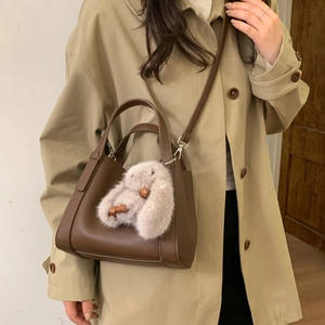 Brown litchi leather bucket bag with plush rabbit charm worn over a khaki trench coat