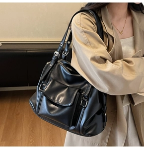 Detail of black leather tote bag with silver metal buckles and adjustable side straps