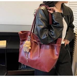 Detail of burgundy faux leather tote bag with decorative buckle and plush bear charm