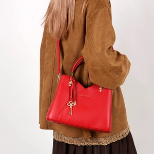 Detail of red bucket bag with gold logo and key charm on a model in a brown coat