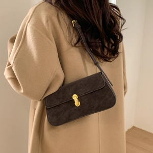 Detail of a dark brown leather underarm bag with gold metal clasp on a camel wool coat