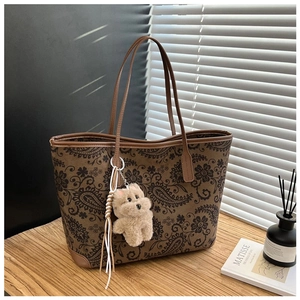 Detail of vintage paisley tote bag featuring premium leather handles and a plush bear charm