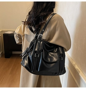 Detail of black tote bag featuring silver buckles and soft leather texture on a model