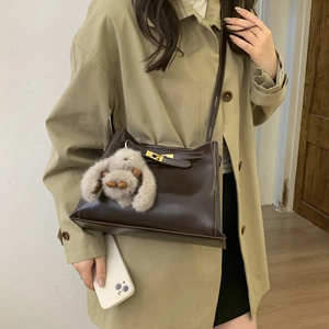 Detail of coffee leather crossbody bag with golden turn-lock and fluffy bunny charm