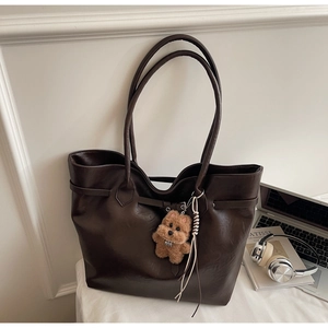 Deep brown faux leather tote bag with plush bear charm in a minimalist lifestyle setting