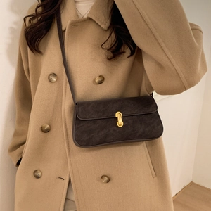 Detail of dark brown leather underarm bag featuring a prominent gold metal twist lock