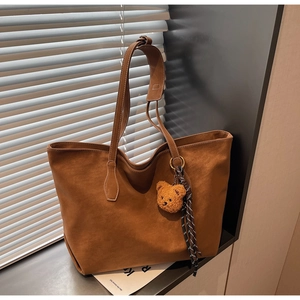 Détail du cabas en daim caramel avec breloque ours en peluche et ruban rayé décoratif