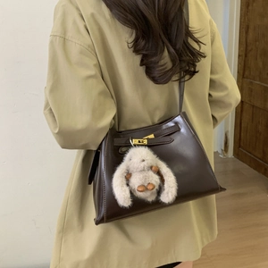 Detail of dark brown leather bucket bag with gold clasp and grey plush rabbit charm