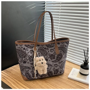 Close-up of vintage paisley tote bag with brown leather handles and plush bear charm