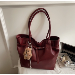 Close-up of burgundy tote bag with leather texture, belt buckle, and plush charm