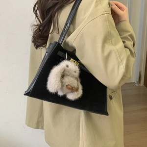 Model wearing a black leather trapezoid bag with golden lock and grey rabbit charm