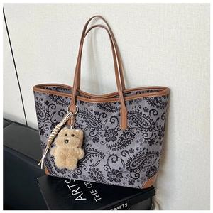 Detail of vintage paisley tote bag with brown leather trim and a cute plush bear charm